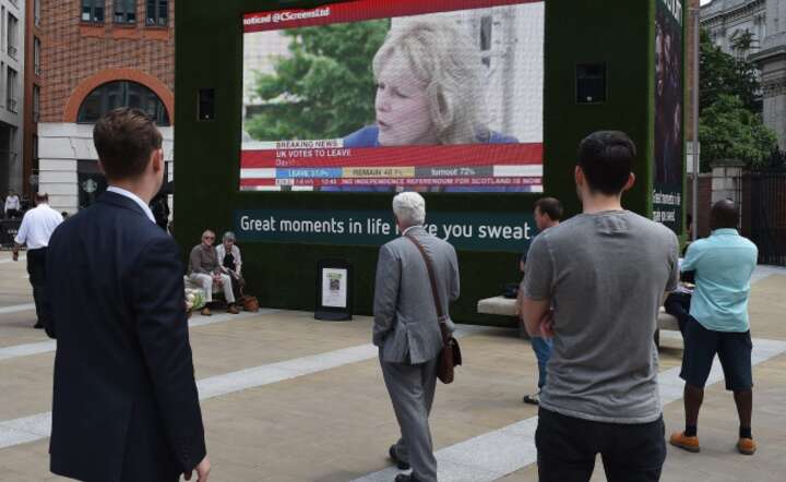Mieszkańcy Londynu śledzą doniesienia o sytuacji po referendum na ulicznych telebimach, fot. PAP/EPA/ANDY RAIN