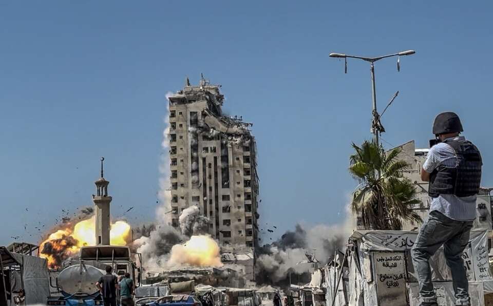 Dziennikarz filmuje izraelski atak lotniczy na wieżę Mushtaha na zachodzie miasta Gaza / autor: 	PAP/EPA