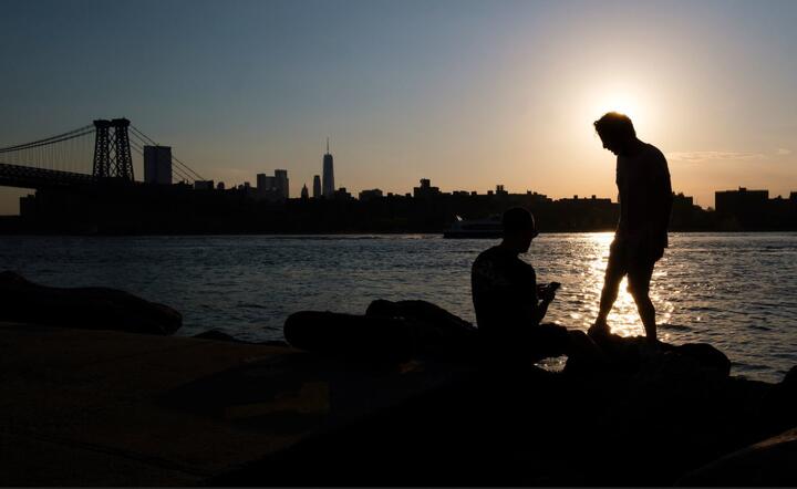 Ludzie siedzący niedaleko East River. W tle Manhattan / autor: PAP