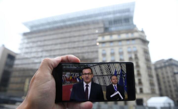  Premier RP Mateusz Morawiecki (na ekranie telefonu L) i minister do spraw Unii Europejskie Konrad Szymański (na ekranie telefonu P) w pierwszym dniu szczytu UE w Brukseli, 17 bm. / autor: PAP/Radek Pietruszka