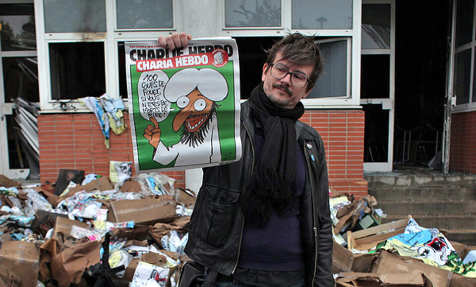 fot. dziennikarz prezentujący okładkę wcześniejszego numeru Charlie Hebdo na tle zdewastowanej redakcji, PAP/EPA