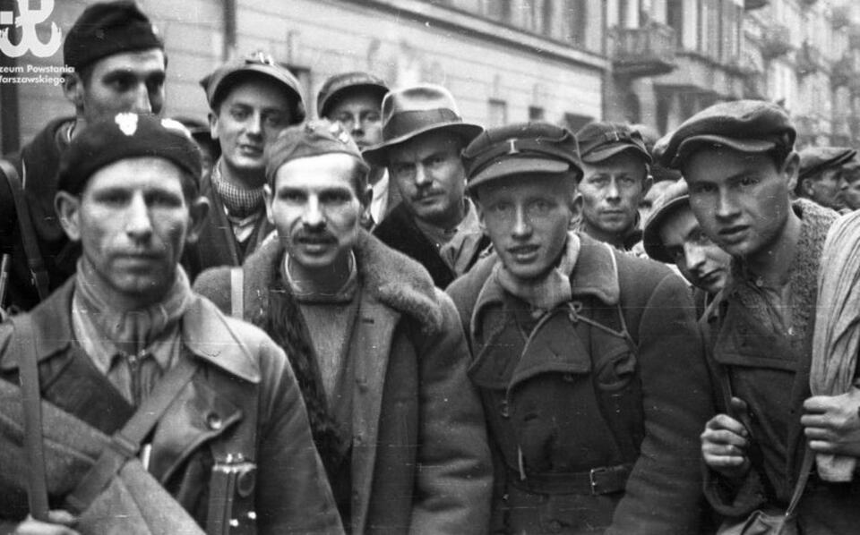 Fotografia z Powstania Warszawskiego. Kolumna powstańców czekająca na wymarsz do niewoli na ul. Śniadeckich. W tle za powstańcami widoczny gmach Towarzystwa Naukowego Warszawskiego przy Śniadeckich 8. Fot. Muzeum Powstania Warszawskiego
