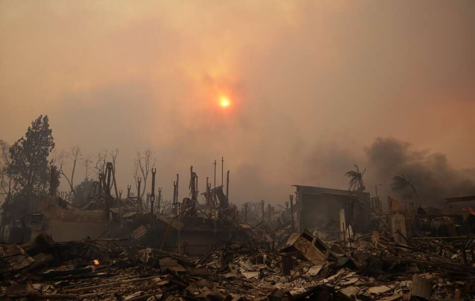 Słońce przebija się przez dym nad ruinami domów po pożarze w dzielnicy Pacific Palisades w Los Angeles / autor: PAP/EPA/ALLISON DINNER