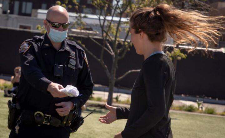 Policjant rozdaje maski w Domino Park w dzielnicy Brooklyn w Nowym Jorku w USA w dniu 2 maja 2020 r. Nowy Jork pozostaje epicentrum epidemii koronawirusa w USA. / autor: PAP/EPA/GARY HE