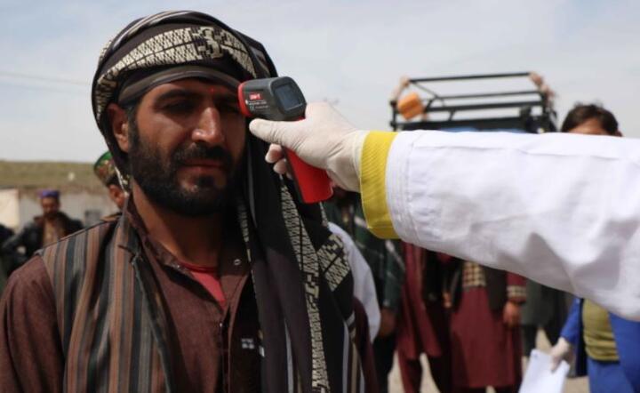 Pracownik służby zdrowia sprawdza temperaturę, aby zapobiec rozprzestrzenianiu się koronawirusa SARS-CoV-2, podczas blokady w Heracie w Afganistanie. / autor: PAP/EPA/JALIL REZAYEE