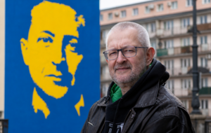 na zdjęciu Rafał Ziemkiewicz, w tle wizerunek Wołodymyra  Zełenskiego na plakacie (grafika wygenerowana przy użyciu narzędzi AI) / autor: Fratria/wPolityce.pl