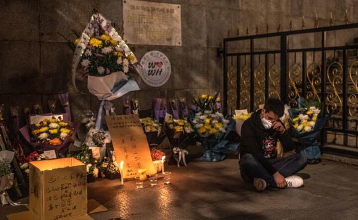 Wolontariusz twierdzący, że jego przyjaciel zmarł na Covid-19, siedzi obok kwiatów umieszczonych w pamięci ofiar Covid-19 w Wuhan, Chiny, 4 kwietnia 2020 r. / autor: PAP / EPA.