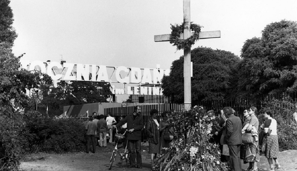 Drewniany krzyż, ustawiony przez strajkujących w miejscu, gdzie zginęli stoczniowcy w grudniu 1970 roku. Jednym z żądań strajkowych była budowa Pomnika Poległych Stoczniowców, który został odsłonięty w grudniu 1980. W głębi Brama nr 2 Stoczni Gdańskiej / autor: Małgorzata Lewandowska - http://ecs.gda.pl/commons.wikimedia.org/CC BY-SA 3.0 pl/