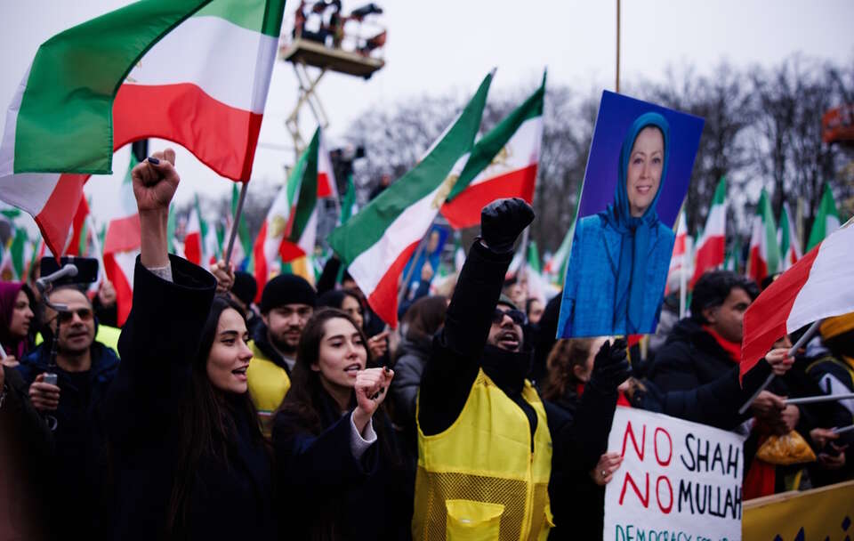 Wolny Iran – wiec w Berlinie. Uczestnicy krzyczą hasła i trzymają transparent z napisem „Nie dla szacha, nie dla mułły, demokracja dla Iranu”. Obok portretu liderki Ruchu Oporu Iranu. / autor: PAP/EPA/CLEMENS BILAN